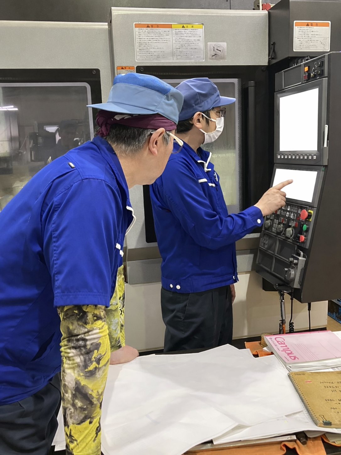 操作盤の前で後輩に機械操作を教える先輩技術者